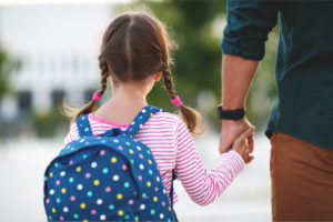 A father holding his daughter’s hand as they walk.