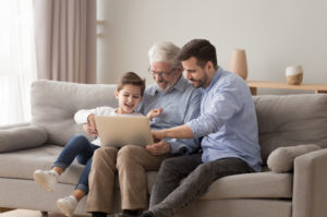 A grandfather using a laptop with his adult son and grandchild.