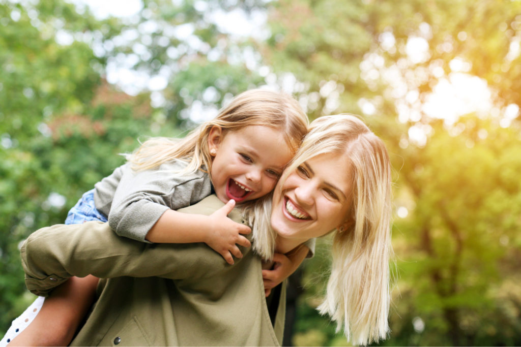 A mother giving her daughter a piggyback, and laughing together.