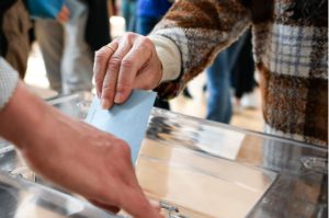 A person putting a ballot paper into a box.