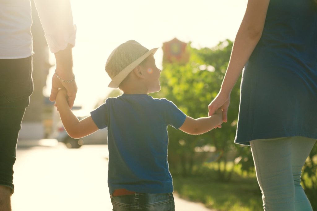 A family with a young child holding hands outdoors.