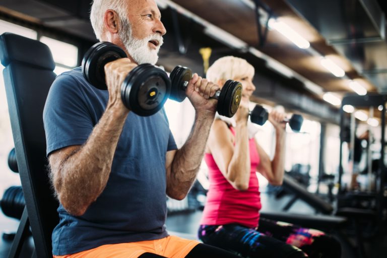 Two people in their 60s using weights in a gym.