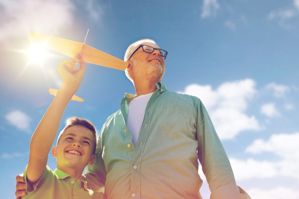 A grandfather and grandson playing with a toy plane outdoors.