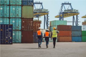 Workers walking through a shipping cargo container terminal depot.
